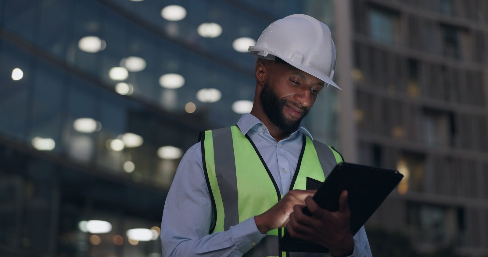 black-man-engineer-city-building-with-tablet-online-inspection-safety-protocol-architecture-late-night-male-person-hardhat-construction-project-with-deadline-internet-urban-min